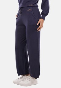 Pantaloni a gamba larga blu navy in morbido tessuto con vita regolabile, dotati di tasche frontali e logo "YESZEE" in oro sulla cintura.