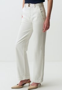 Pantalons larges blancs en denim, dotés de deux boutons, poches avant, coutures contrastées et une légère texture.
