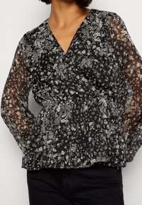 Czarna bluzka w kwiaty z prześwitującymi długimi rękawami, dekoltem w serek, marszczoną talią oraz misternym białym wzorem kwiatowym na całej powierzchni. Miękki, lekki materiał.