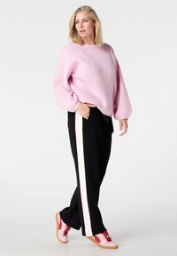 Pull rose en maille avec manches bouffantes, pantalon noir avec bandes blanches sur les côtés, et baskets roses avec lacets rouges.