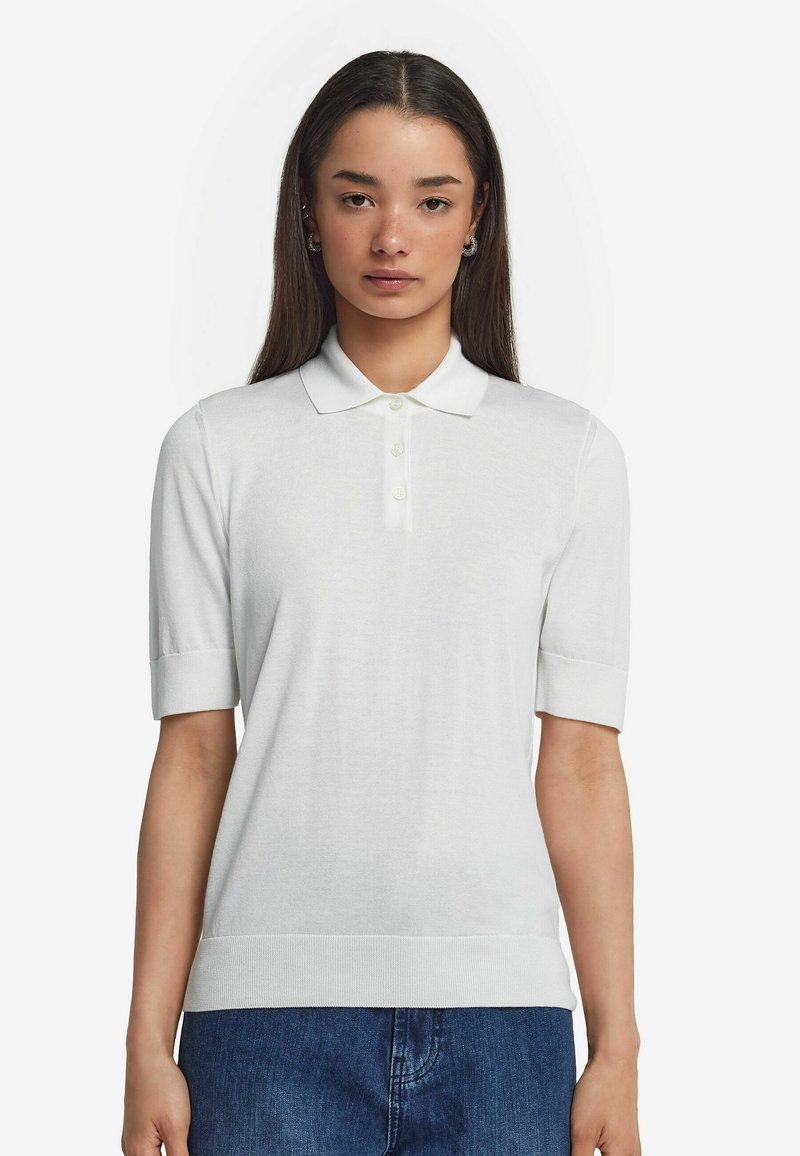 Vit kortärmad polo skjorta med klassisk krage, treknapplås och strukturerad stickad tyg, i kombination med mörkblå denim.