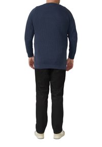 Dunkelblauer Rippsweater mit langen Ärmeln und rundem Ausschnitt, kombiniert mit schwarzer Hose und hellen Sneakers. Rückansicht gezeigt.