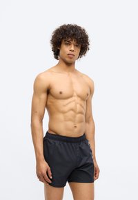 Melnas peldbikses ar elastīgu jostu, ar gludu auduma tekstūru. Modelis ar muskulētu uzbūvi un cirtainiem matiem, bez krekliem.