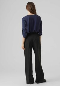 Haut à manches longues marine associé à un pantalon large à taille haute noir. Texture lisse, coupe décontractée et détails de couture subtils visibles.