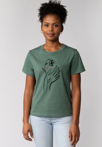 Grünes Baumwoll-T-Shirt mit einer schwarzen Linienzeichnung einer Hand, die eine Blume und ein Herz hält. Klassischer Rundhalsausschnitt, kurze Ärmel, legere Passform.