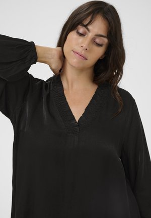 Svart blus i slätt tyg med V-ringning och volangdetaljer samt puffärmar. Inga mönster eller metalldetaljer synliga.