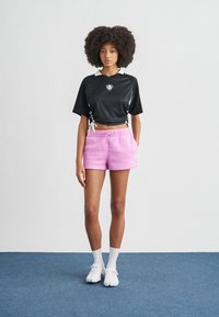 Μαύρο κοντομάνικο τζέρσεϊ με λευκό γιακά και κορδόνι, σετ με ροζ σορτς, λευκές κάλτσες και λευκά παπούτσια με υφασμένη σόλα.