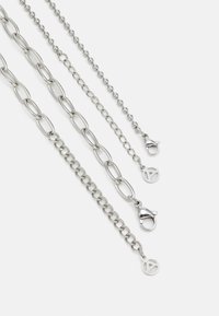 Silver chain accessory featuring varying link styles: elongated links, spherical beads, and a clasp with a decorative charm.
