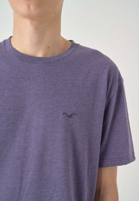 Lila Kurzarm-T-Shirt aus weichem Stoff mit Rundhalsausschnitt und kleinem gesticktem Logo auf der Brust. Glatte Textur und lockere Passform.