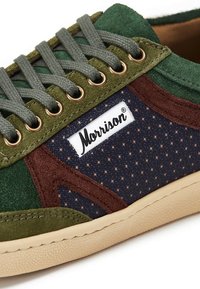 Zapatillas de ante verde y marrón con panel de tela azul marino que presenta un patrón de estrellas. Incluye cordones grises, ojales redondos y etiqueta de logo.