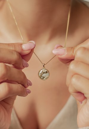 Goldkette mit einem runden Anhänger, der ein detailliertes Wellenmuster zeigt, vor einem perlmuttartigen Hintergrund, umrahmt von einem gedrehten Seilrand.