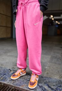 Rosa svettbyxor med dragsko i midjan och sidofickor, kombinerade med orange och bruna Nike-sneakers med vita accenter.