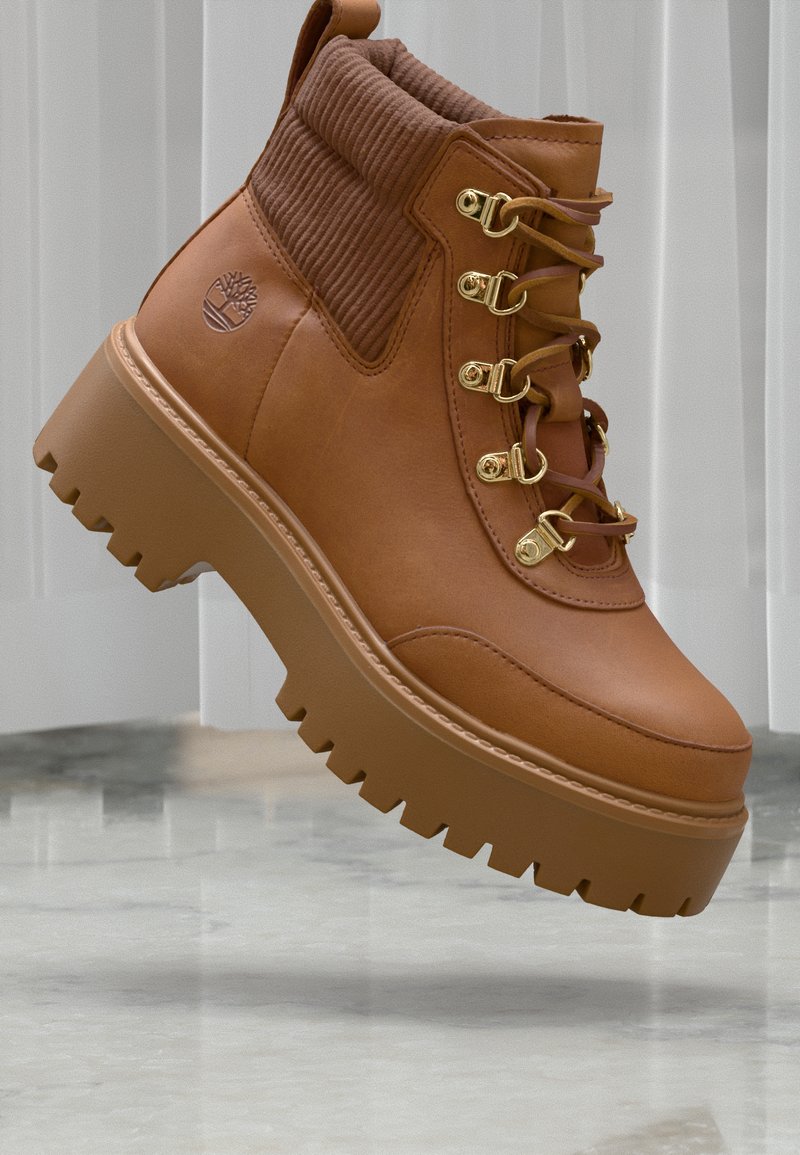 Bottines en cuir marron avec tige en textile à côtes, garnitures en or et semelle épaisse à motif. Présente un détail de logo sur le côté.