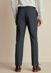 Pantalons navy sur mesure avec une texture subtile, présentant des accents en cuir marron sur les poches arrière et un design à jambes droites.