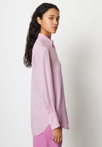 Camicia a maniche lunghe di un rosa chiaro con colletto, polsini con bottoni e orlo arrotondato. Tessuto morbido con una leggera lucentezza.