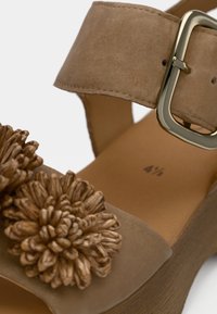 Μπεζ σανδάλι με πλατφόρμα και φαρδιά λουράκι στον αστράγαλο, χρυσή πόρπη και διακοσμητικά λουλουδάτα στοιχεία από υφασμάτινο υλικό στην περιοχή των δαχτύλων.