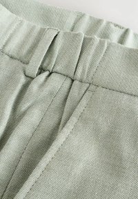 Zeleni teksturirani materijal izbliza, s upletenim uzorkom. Pojas ima šivene akcentne detalje i suptilan sjaj, ističući svoj strukturirani dizajn.