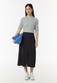Gestreepte blouse met korte mouwen in wit en marineblauw, gecombineerd met een zwarte midi rok met een split aan de voorkant. Houdt een blauwe tas vast en draagt lichte sneakers.