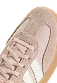 Zapatilla de ante rosa con acentos de malla, puntera redonda, cordones planos y detalle de rayas blancas en el costado, con suela de goma.