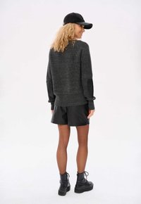 Grauer Strickpullover mit gerippten Bündchen und schwarzen Lederpatches an den Ärmeln, kombiniert mit schwarzen Lederhosen und schwarzen Schnürstiefeln.