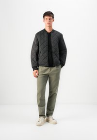 Giacca bomber nera trapuntata con colletto a coste, abbinata a pantaloni dritti verde oliva e sneaker crema. Design minimalista e vestibilità strutturata.