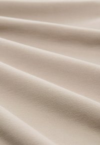 Tela de algodón beige con una textura suave y mate, que presenta pliegues suaves y fluidos y sutiles patrones de tejido por toda su superficie.