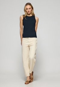 Marinblå ribbad ärmlös topp, krämfärgade avslappnade byxor och bruna klacksandaler. Anmärkningsvärda detaljer inkluderar en liten logotyp på toppen.