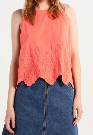 Coral sleeveless top with scalloped embroidered hem, featuring paisley patterns and textured fabric, paired with a denim skirt.