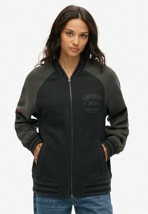 Veste zippée noire et grise avec un col et des poignets côtelés, dotée de poches latérales et de détails de logo discrets sur le devant.