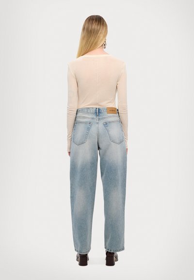Light beige long-sleeve top paired with high-waisted, faded blue denim jeans featuring a tan leather patch on the back.
