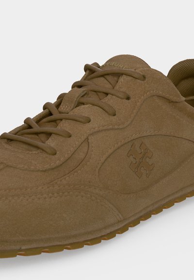 Sneaker en daim marron avec lacets assortis, semelle en caoutchouc et logo géométrique brodé sur le panneau latéral près du talon.