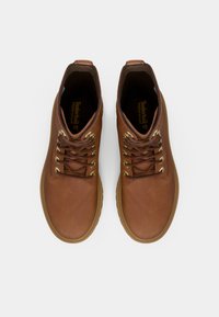 Par av brune lær lace-up vanntette støvler med tan såler sett ovenfra på hvit bakgrunn.