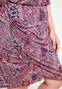 Vestido multicolorido con un patrón de paisley en tonos rojos, azules y crema. La tela tiene una textura suave con detalles drapeados.