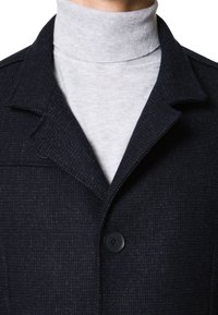 Ciemnoniebieski wełniany płaszcz o teksturowanym wykończeniu, z pojedynczym zapięciem na guzik i wyrazistym kołnierzem, nałożony na jasnoszary golf.
