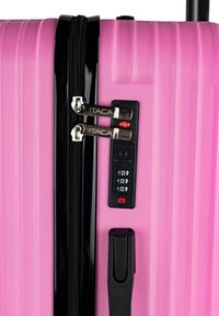 Equipaje rosa con un acabado texturizado, que cuenta con una cremallera negra, cerradura de combinación y dos tiradores metálicos de la cremallera etiquetados como "ITACA".