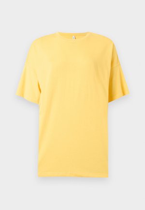 Gele oversized T-shirt met korte mouwen en ronde hals, plat neergelegd op een lichtgrijze achtergrond.