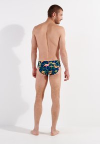 Herren-Schwimmbrillen in marineblau mit einem lebhaften Blumenmuster, das pinke Flamingos und gelbe Lilien zeigt, aus elastischem Stoff gefertigt.