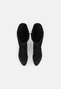 Bottes ankle en suede noir avec un design flou, un bout pointu et une fermeture éclair latérale pour un enfilage facile. La texture est lisse et douce.