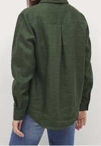 Camicia di lino verde scuro con piega sul retro, polsini abbottonati e orlo curvo. Tessuto testurizzato con una vestibilità rilassata.