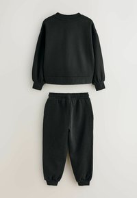Sudadera negra de manga larga y pantalones jogger a juego con cintura elástica dispuestos sobre un fondo claro.