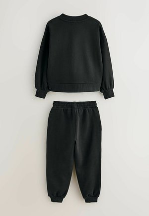 Schwarzes Langarm-Sweatshirt und passende Jogginghosen mit elastischem Bund flach auf einem hellen Hintergrund ausgelegt.
