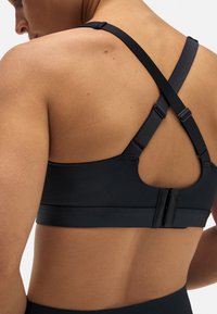 Sujeción deportiva negra con diseño de espalda nadadora, correas ajustables y cierre de gancho en la parte posterior, fabricada en material suave y elástico.