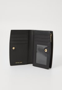 Zwarte leren portemonnee met meerdere kaartsleuven, een doorzichtige ID-venster en een goudkleurige drukknoop. Bevat een geperst merkteken. Compact ontwerp.