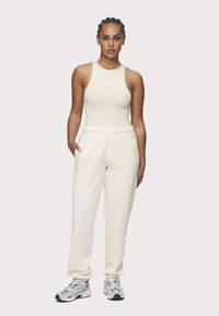 Body senza maniche beige con logo, abbinato a joggers colore crema con vita elastica e tasche, completato da sneakers grigie.