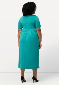 Vestido midi turquesa con mangas cortas, cintura elástica y una textura suave, combinado con tacones de aguja negros.