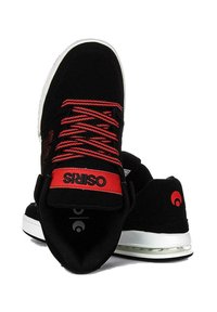 Zapatillas de skate de ante negro con acentos rojos, que cuentan con cuellos acolchados y cordones en contraste, montadas sobre una suela de goma blanca con amortiguación de aire.