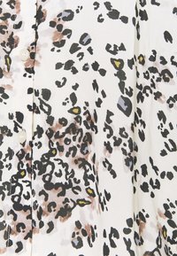 Bluzka w panterkę w kolorze kremowym, z czarnymi i brązowymi plamami oraz żółtymi akcentami. Miękka tkanina, zapinana na guziki, lekki materiał.