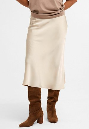 Creme satin midi-nederdel med blød drapering, let udvidet kant, båret med brune ruskind knæhøje støvler. Enkel, glat tekstur.
