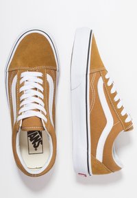 Bruine canvas sneakers met witte accenten, ronde neus, platte veters, rubberen zool en een logo-detail aan de zijkant. Comfortabel, klassiek skateboard schoenontwerp.