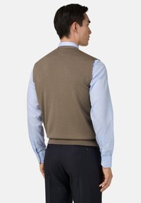 Hnedý pletený sveter cez svetlomodrú košeľu s dlhým rukávom, s okrúhlym výstrihom a hrubým lemom, z pohľadu zozadu.